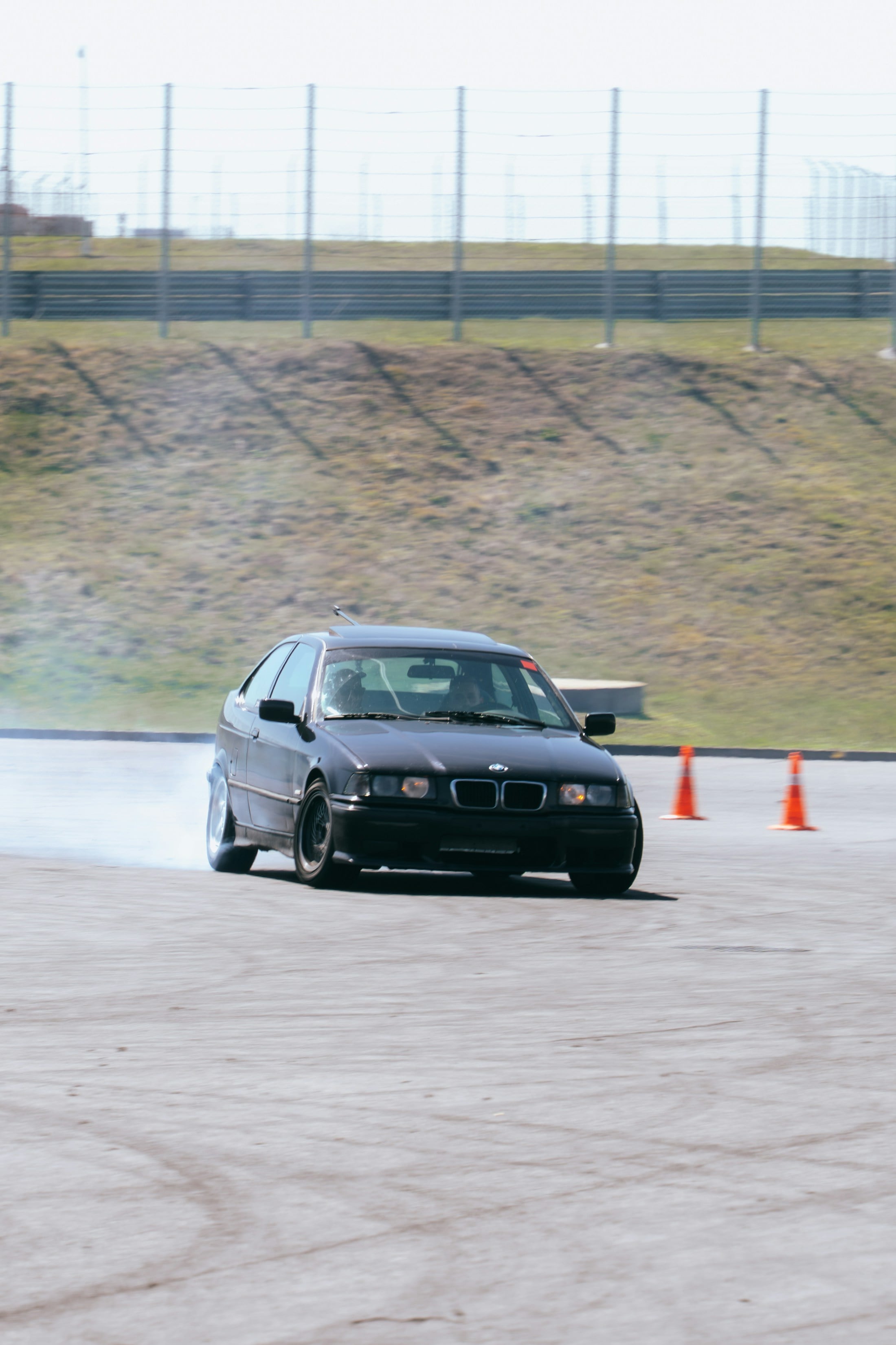 A black drift car sliding through a turn, with tire smoke behind it.